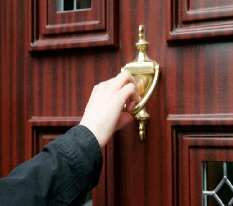 mans hand using door knocker on wood effect upvc door cold calling household